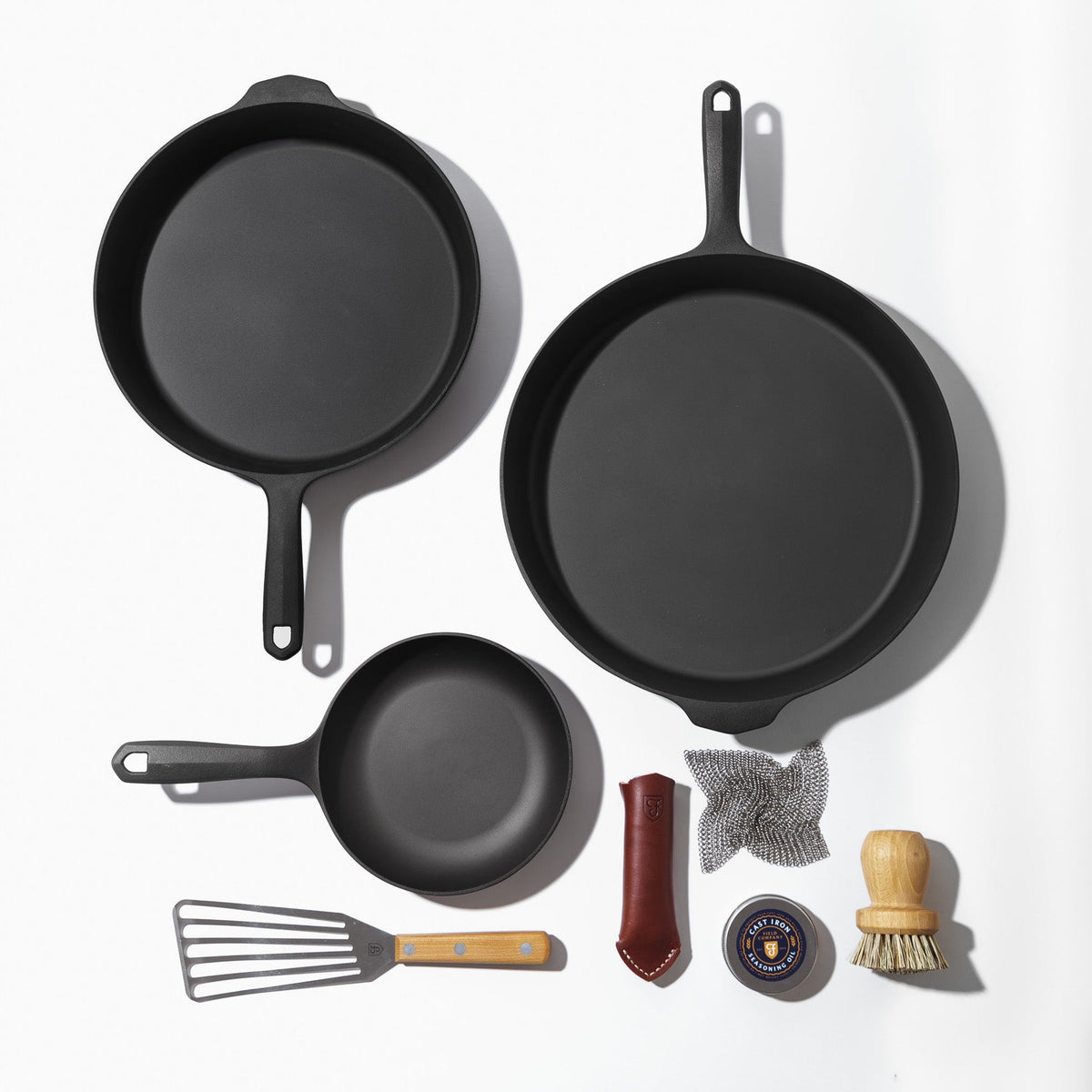 Bird's eye view of all 3 cast iron skillets, cast iron care kit, slotted turner, and mesh scrubber included in kit.