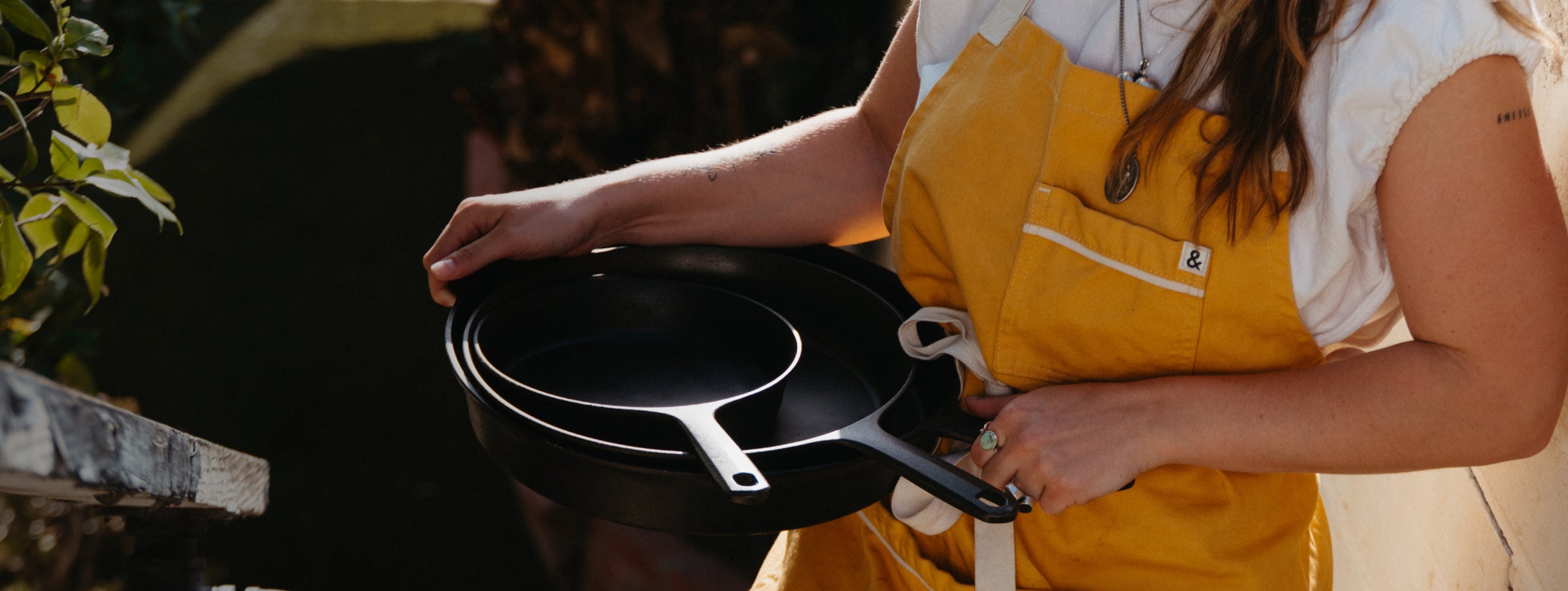 Person in a yellow apron carrying a nested stack of Field Skillets outdoors